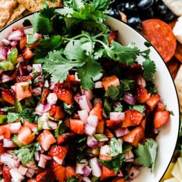 A closeup of strawberry salsa in a white bowl. There is cilantro as garnish to one side.