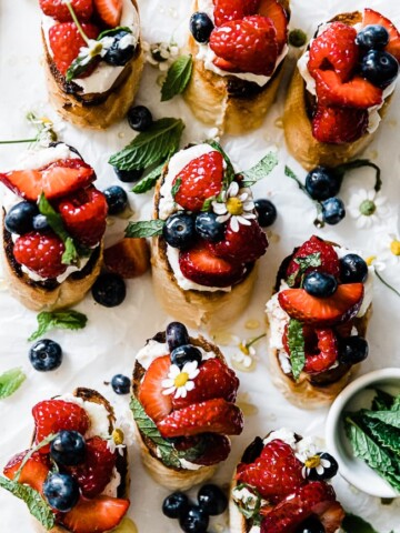 ricotta bruschetta laid on a marble tray. They are garnished with berries and mint.