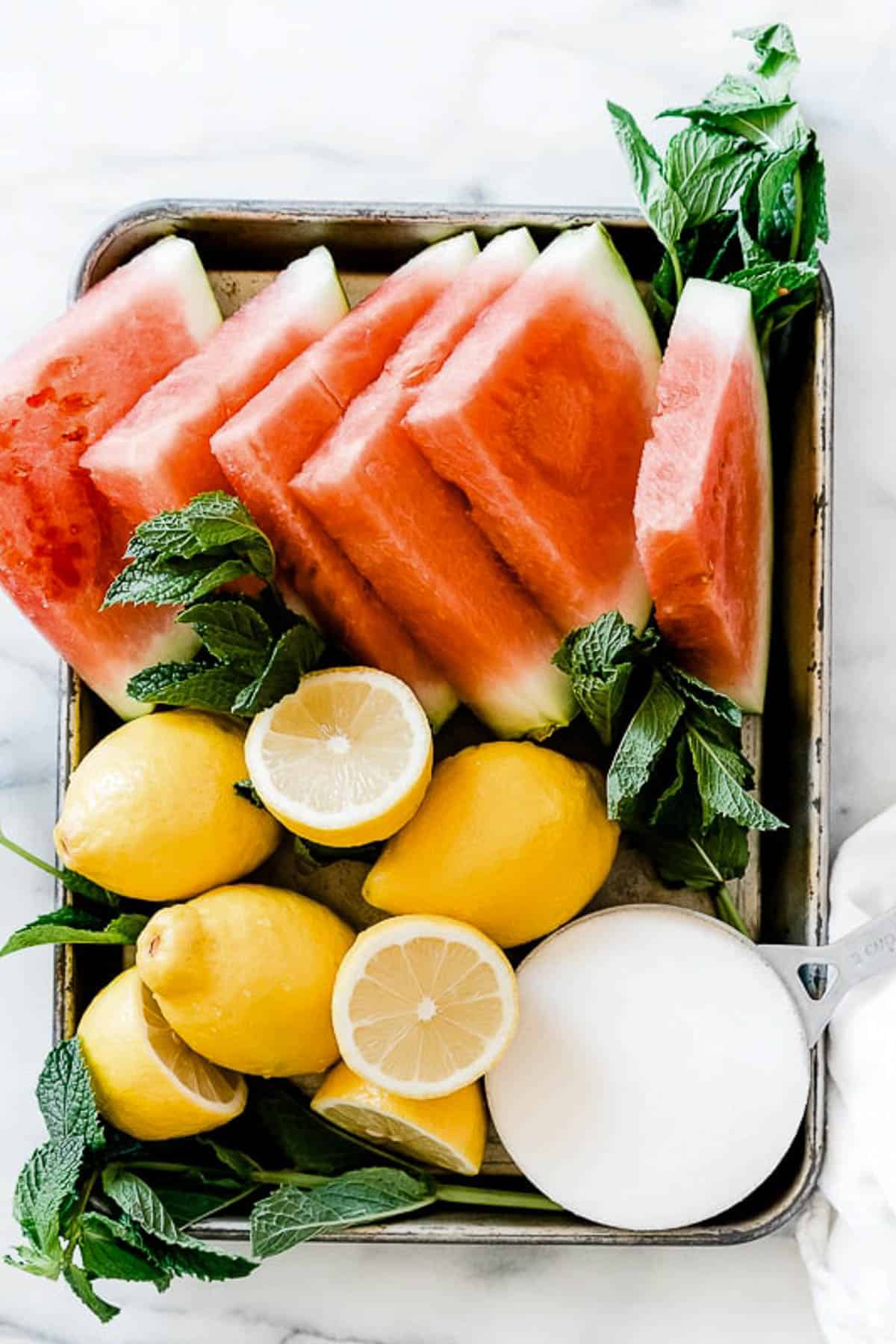 Ingredients needed to make watermelon lemonade on a metal tray.