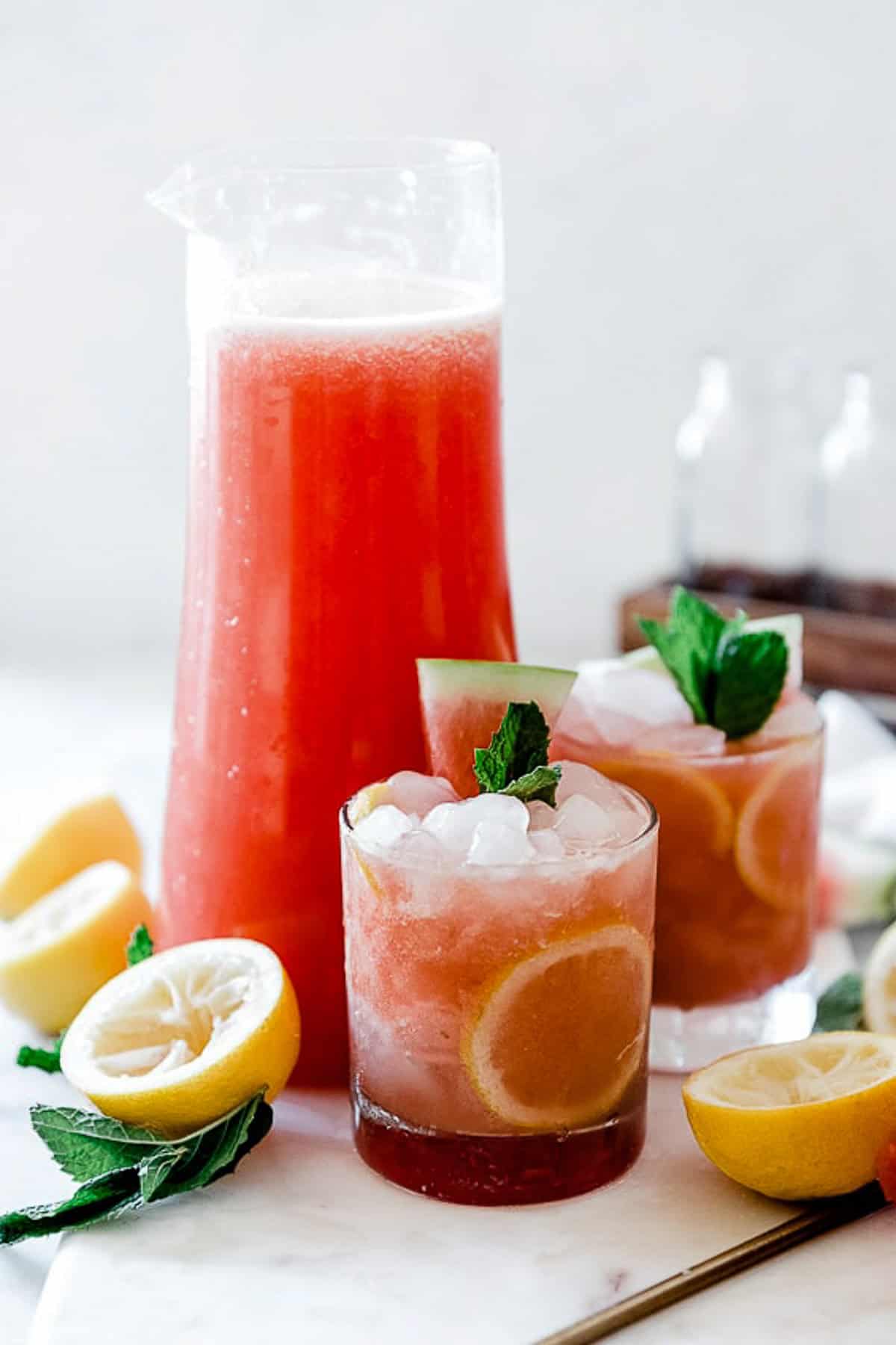 Watermelon lemonade in a tall pitcher with glasses set next to it.