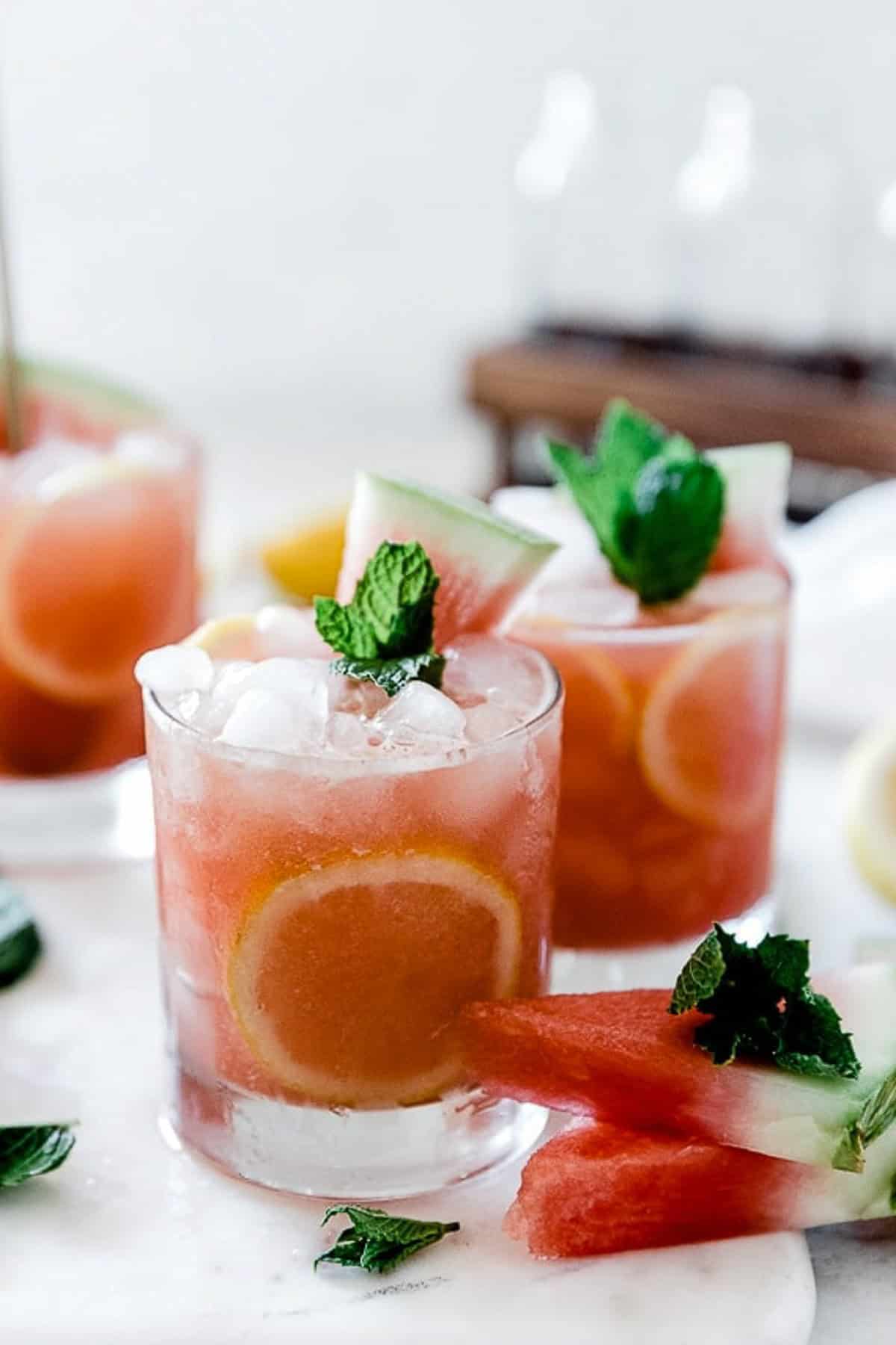 Watermelon lemonade in short glasses, garnished with mint and watermelon on the table.