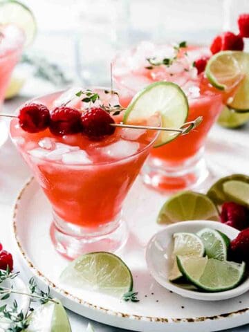 Homemade Raspberry Limeade in martini glasses, surrounded bu lime slices.