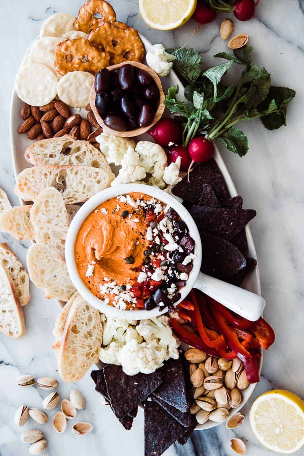 Roasted red pepper hummus on a platter surrounded by bread and veggies.