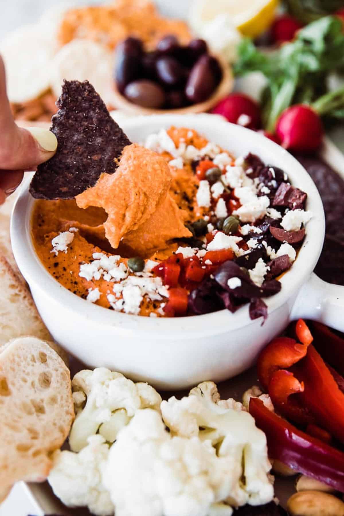 Roasted red pepper hummus being dipped with a blue tortilla chip.