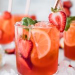 glass of red strawberry basil lemonade with lemons and strawberries as garnish
