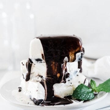 Mud pie recipe on a white plate. There are 3 pieces stacked high and it is covered in chocolate sauce.