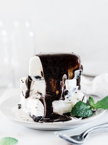 Mud pie recipe on a white plate. There are 3 pieces stacked high and it is covered in chocolate sauce.