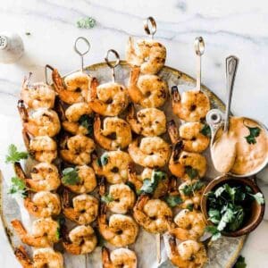 Shrimp on the barbie on skewers served up on a plate.