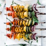Grilled vegetable skewers on a white tray, garnished with basil.