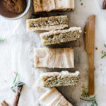 Six zucchini bars lined up next to a wooden knife. There is a bowl of cinnamon to the side.