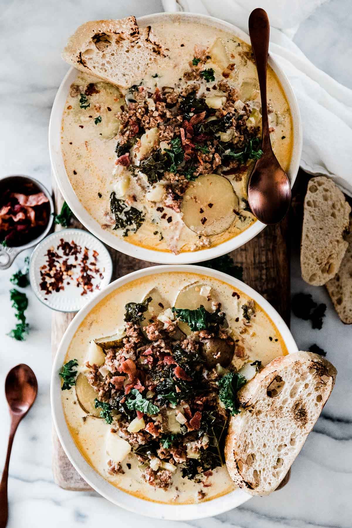 Two bowls of pressure cooker zuppa toscana on a wooden cutting board.