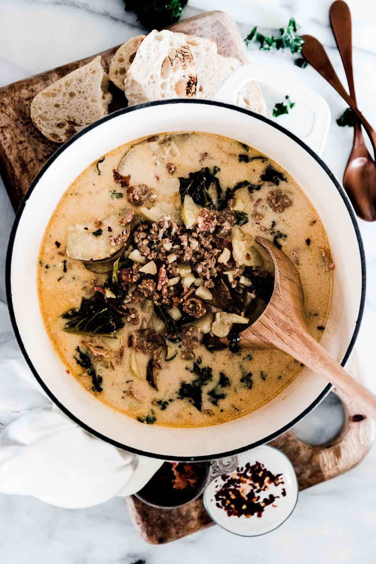 A large pot of instant pot zuppa toscana on a wooden cutting board.