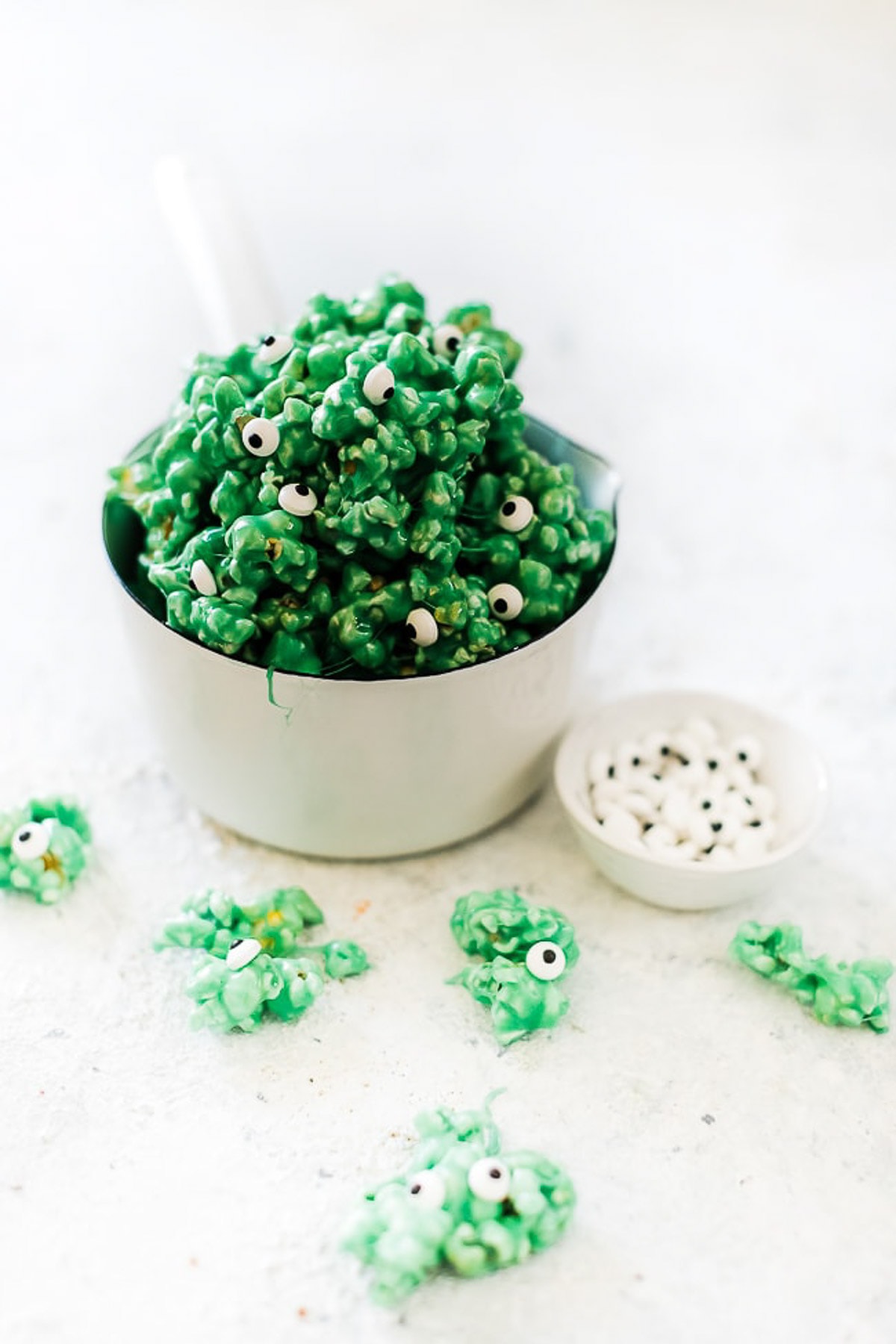 Green halloween popcorn in a white saucepan surrounded by popcorn.