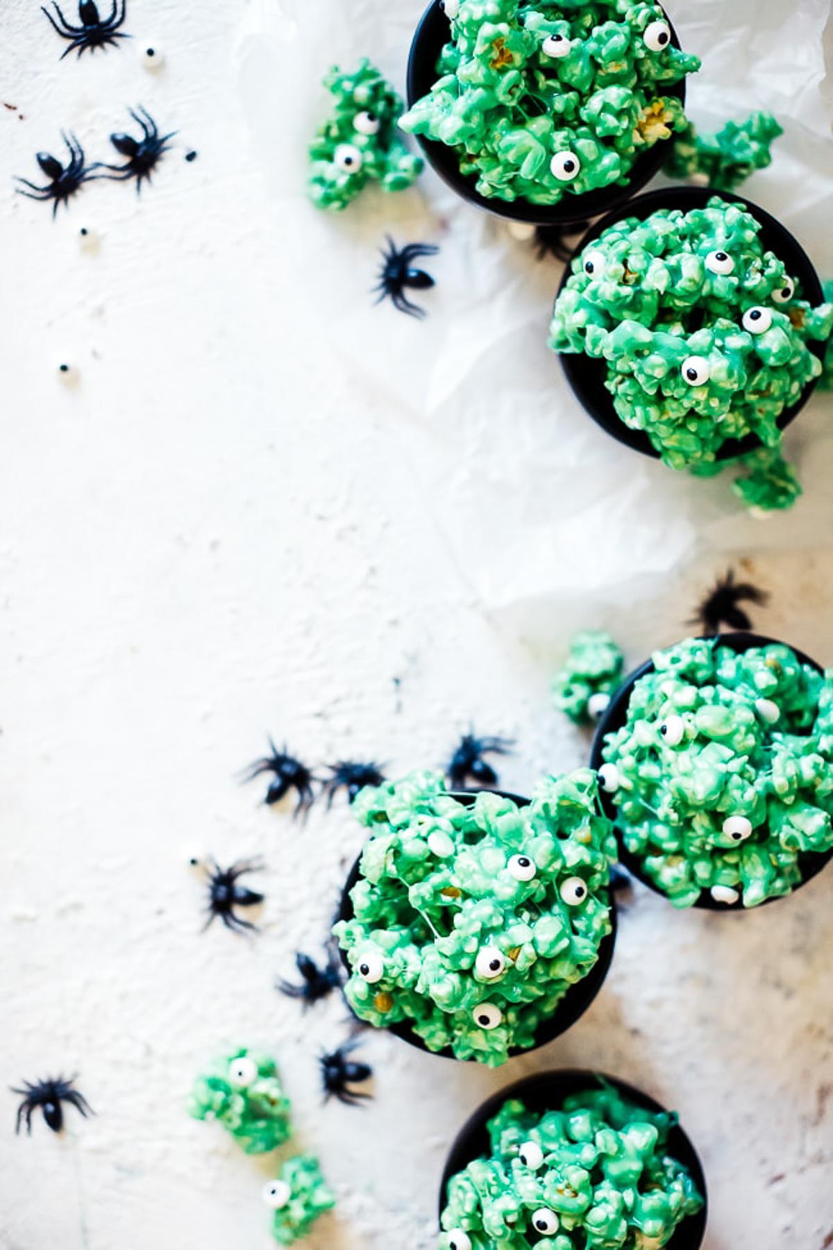 Small black bowls on a white counter, filled with halloween popcorn. There are plastic spiders scattered around.