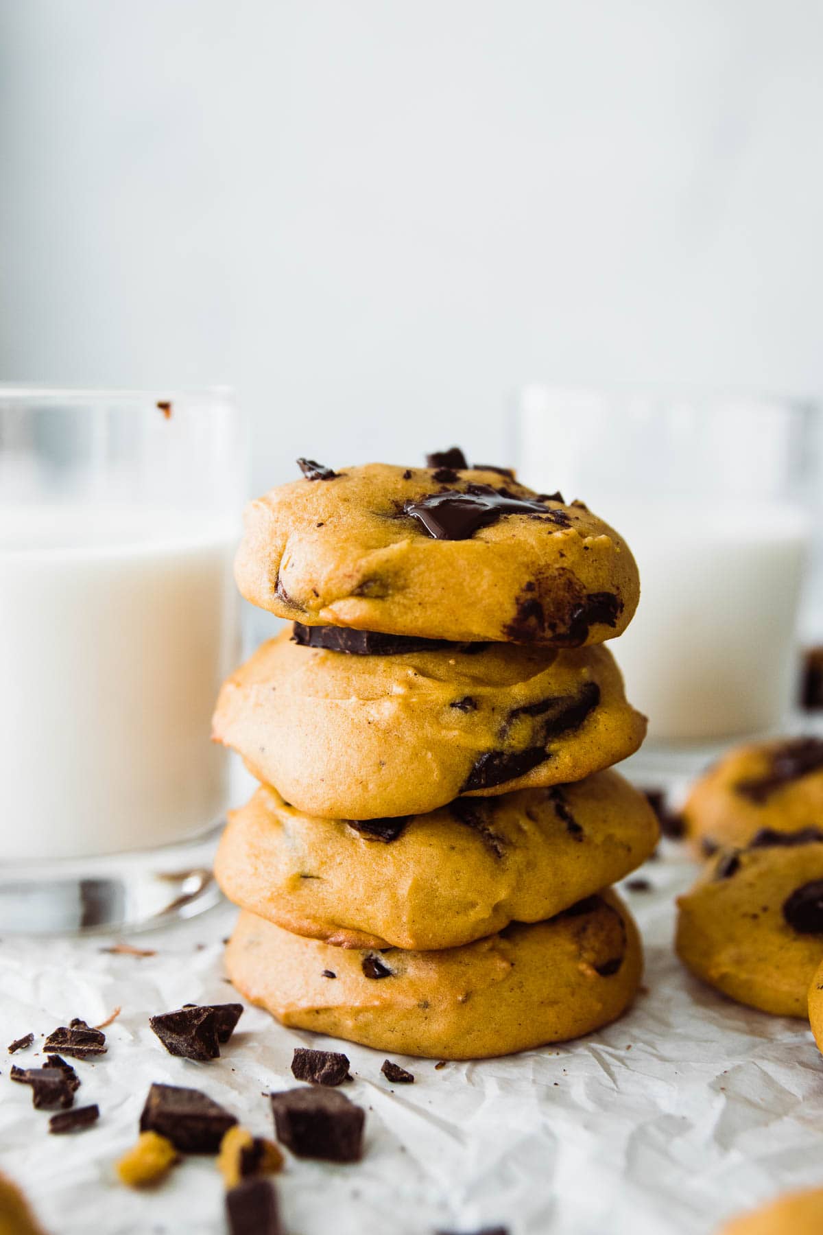 4 cookies stacked with a melted chocolate chip on top and glass of milk to the left. 