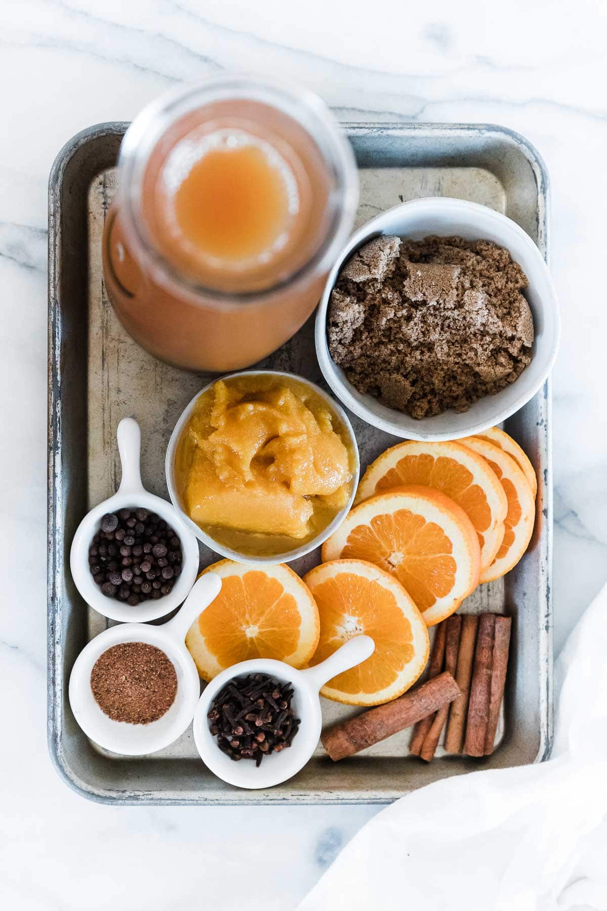 Apple cider, brown sugar, orange slices, and spices on a tray.
