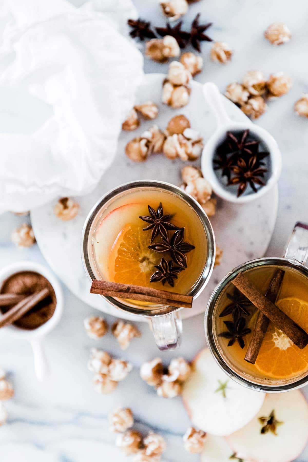 Mulled cider recipe in glass mugs on a marble counter. There is caramel corn scattered around.