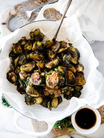 teriyaki roasted Brussel sprouts recipe in a white braiser. There is a bowl of teriyaki to the side.