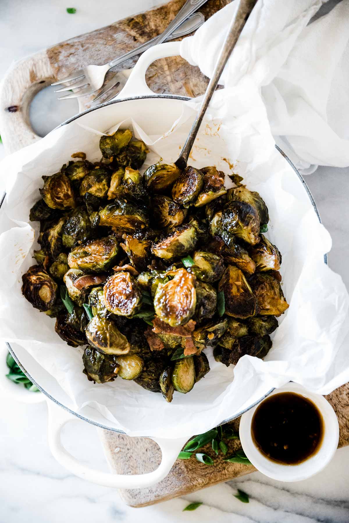 teriyaki roasted Brussel sprouts recipe in a white braiser. There is a bowl of teriyaki to the side.