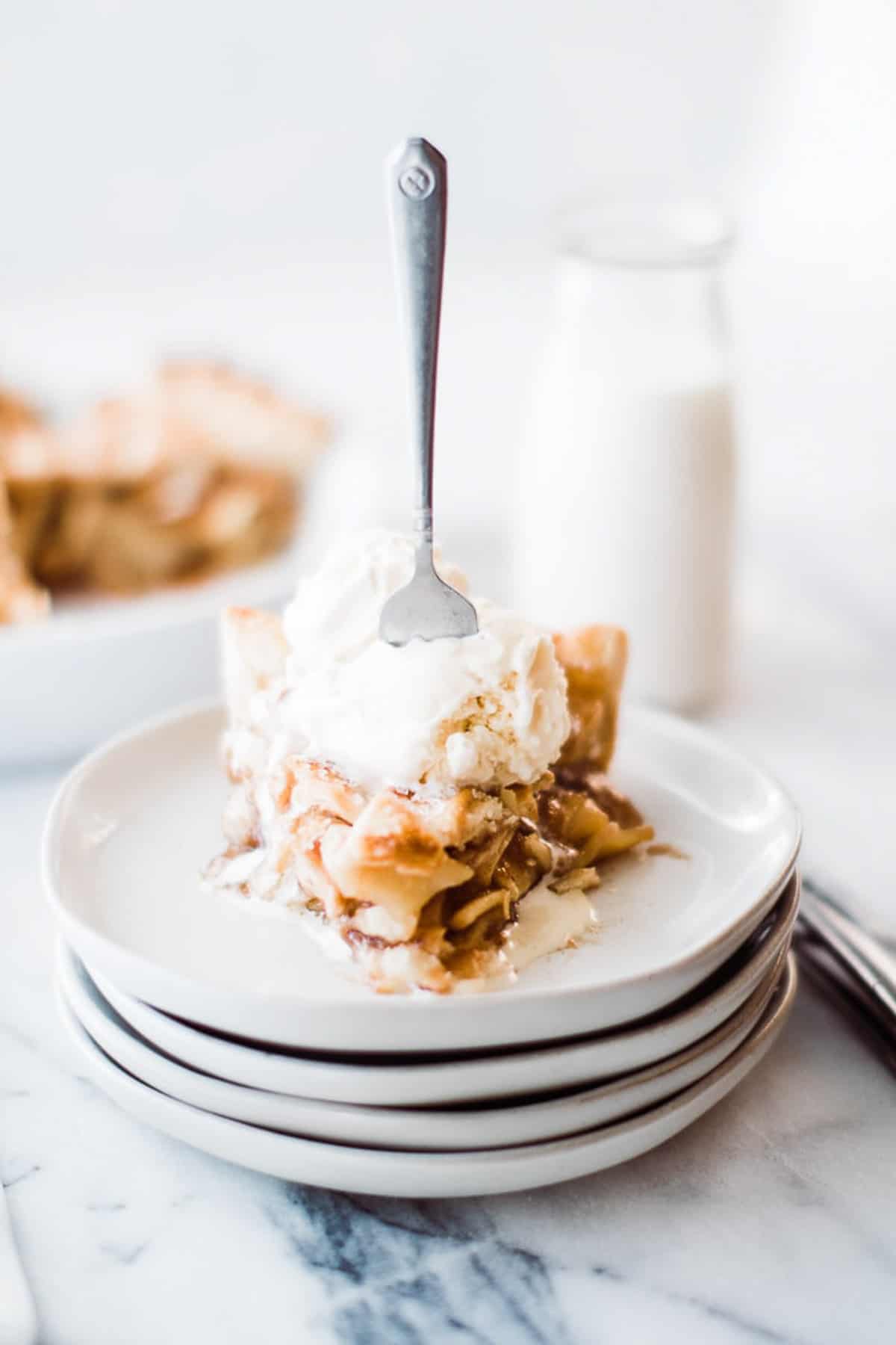 slice of apple pie, with ice cream on a stack of plates