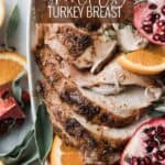 Sliced of juicy smoked turkey on a platter with oranges, herbs and pomegranates.