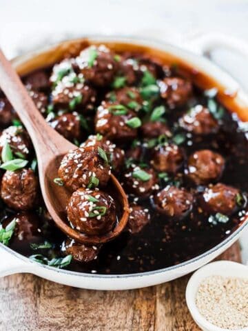 Mongolian meatballs in a white braiser, garnished with sesame seeds and green onion.