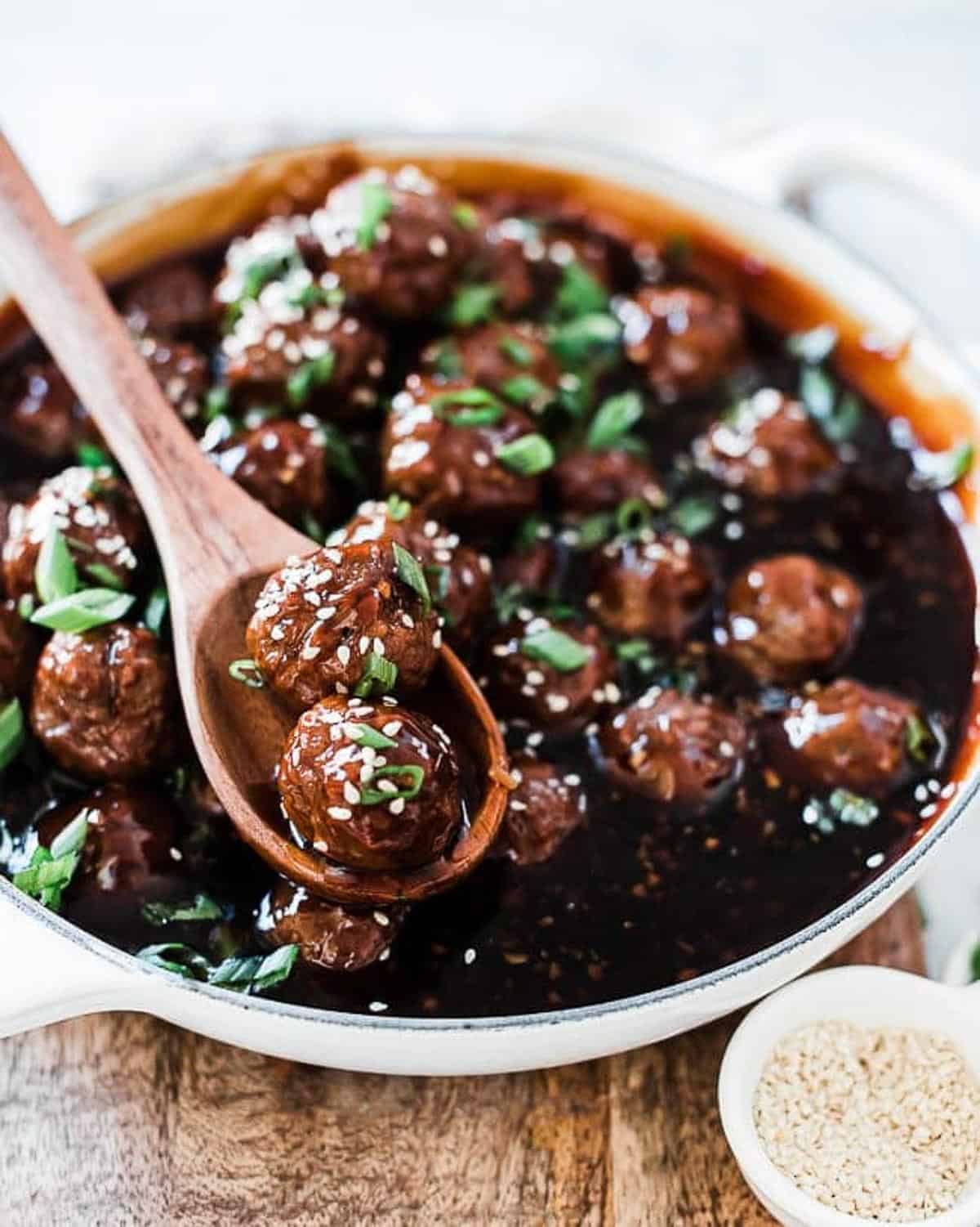 Mongolian meatballs in a white braiser, garnished with sesame seeds and green onion.