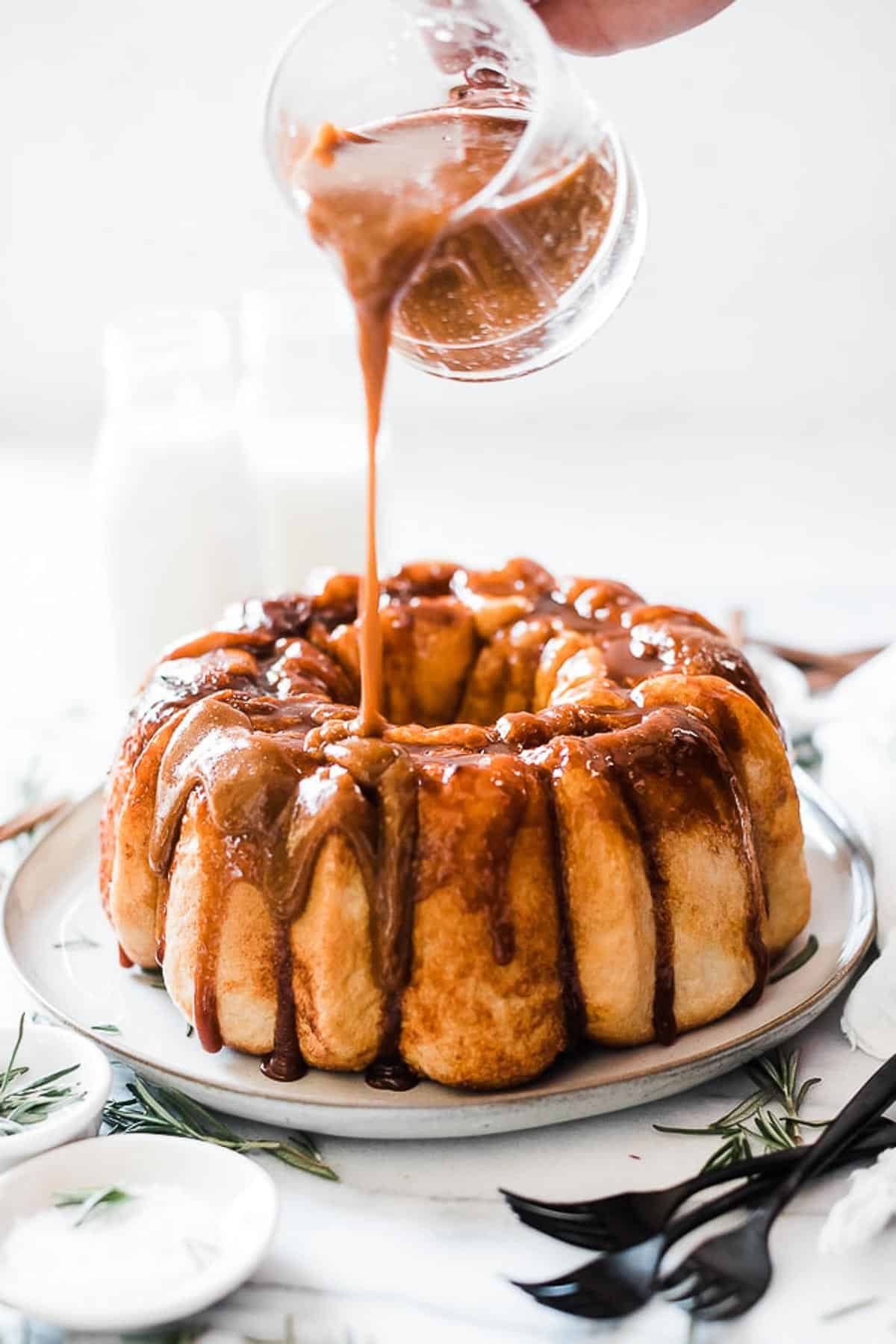 Monkey bread on a cream platter with caramel being pours onto it.