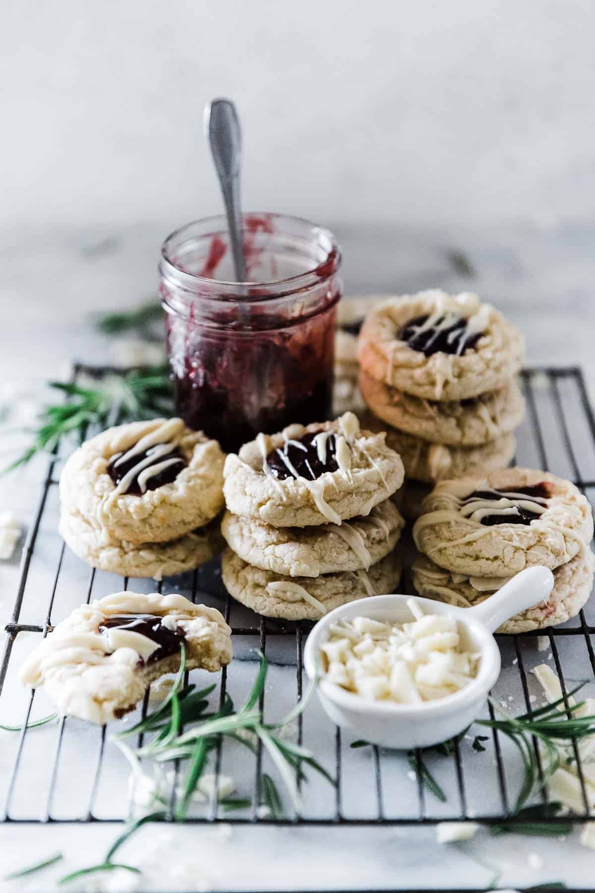 White chocolate raspberry cookies on a cooling rack next to a jar of jam.