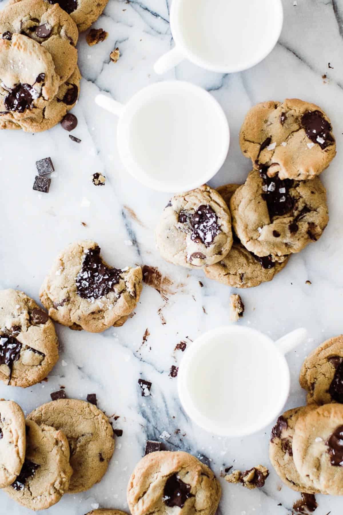 mugs of milk and chocolate chip cookies on marble board