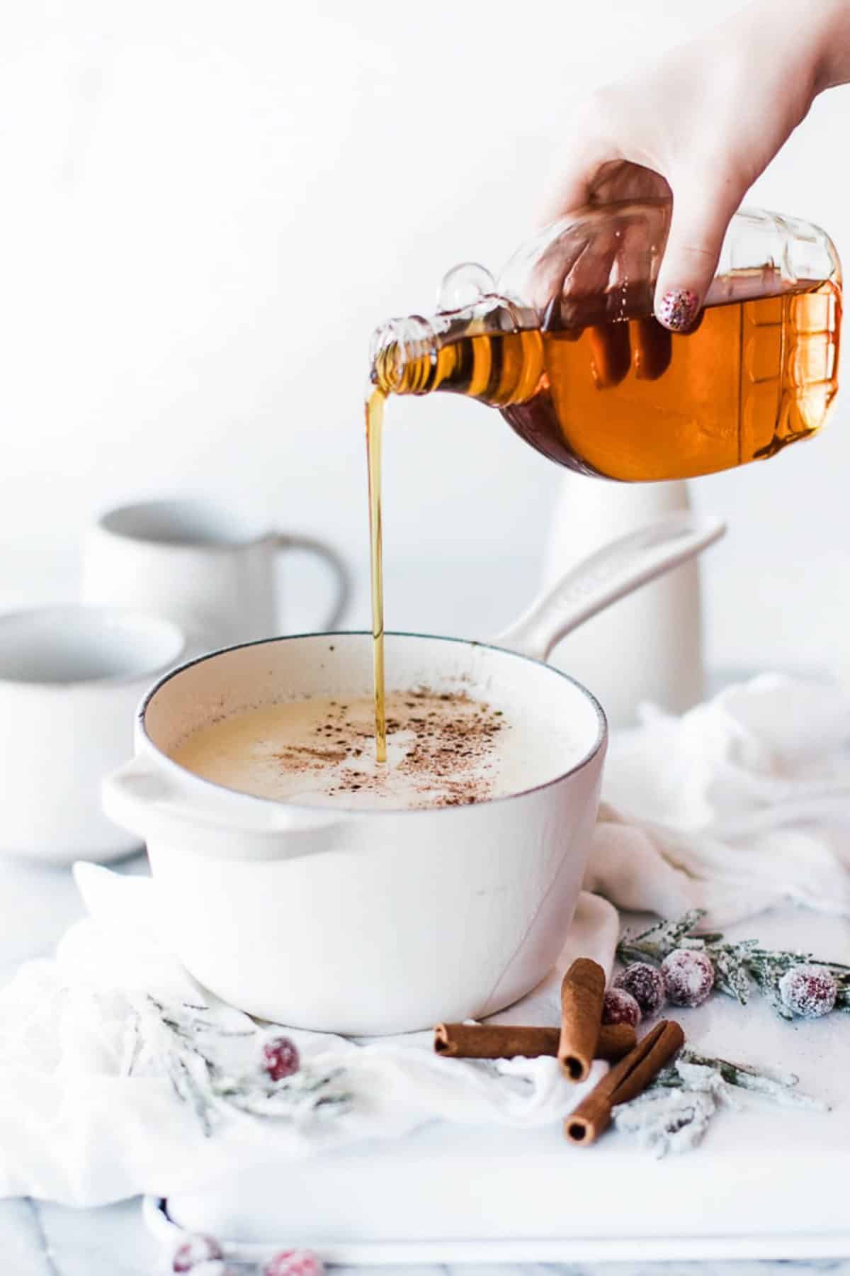 bottle of maple syrup being poured in pan of creamy milk