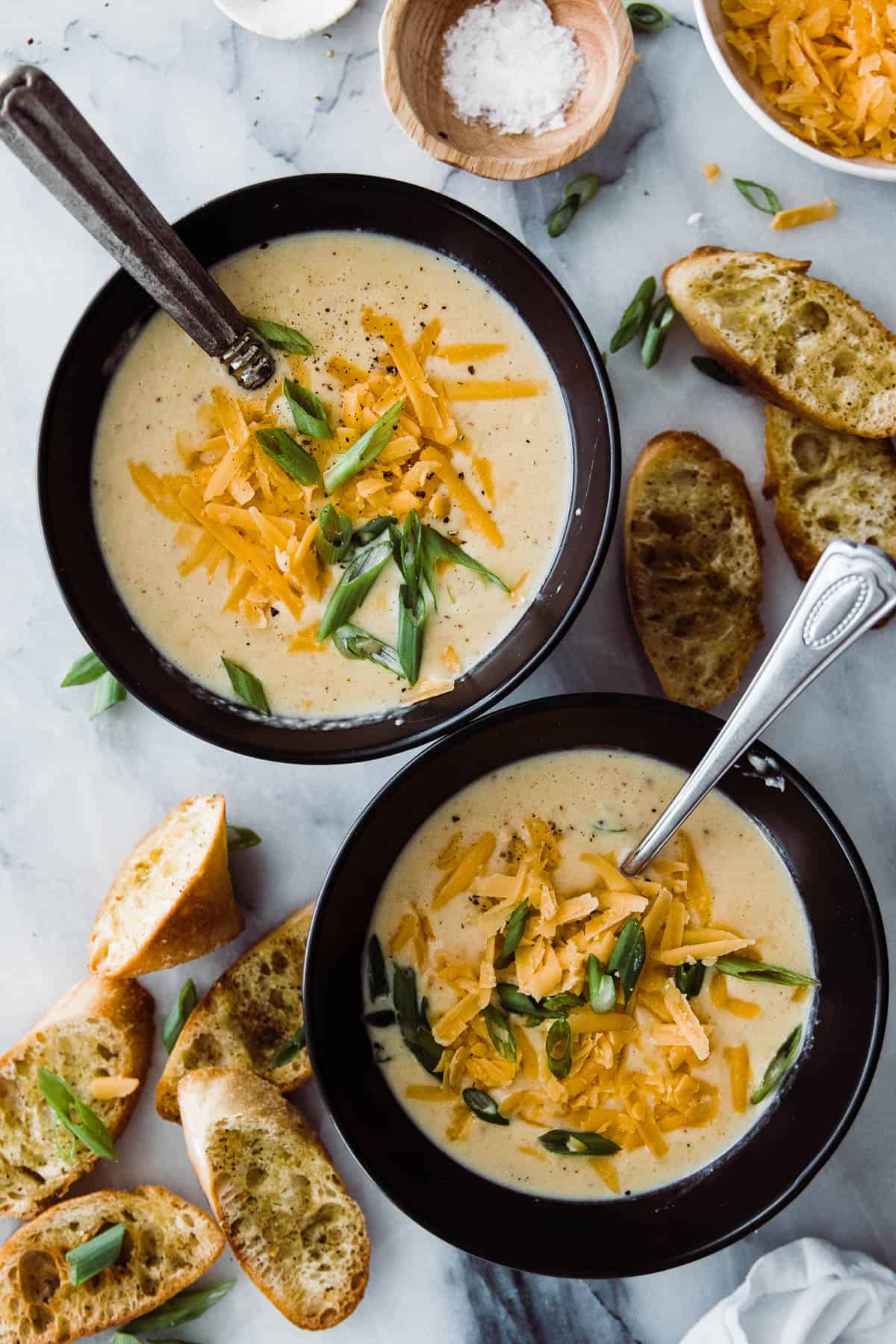 two bowls of cauliflower cheese soup and baguettes around it. 
