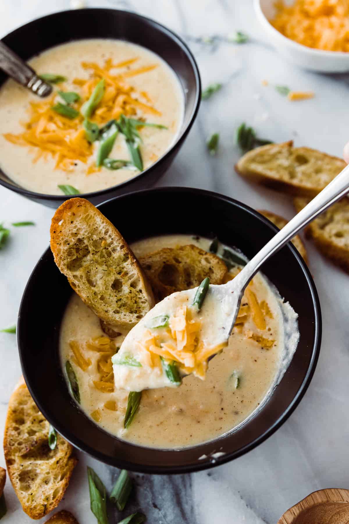 two bowls of soup with a spoon lifting out a spoonful of cheesy soup. 
