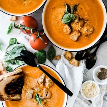 Instant pot tomato soup in white bowls with black rims. They are garnished with croutons and basil.