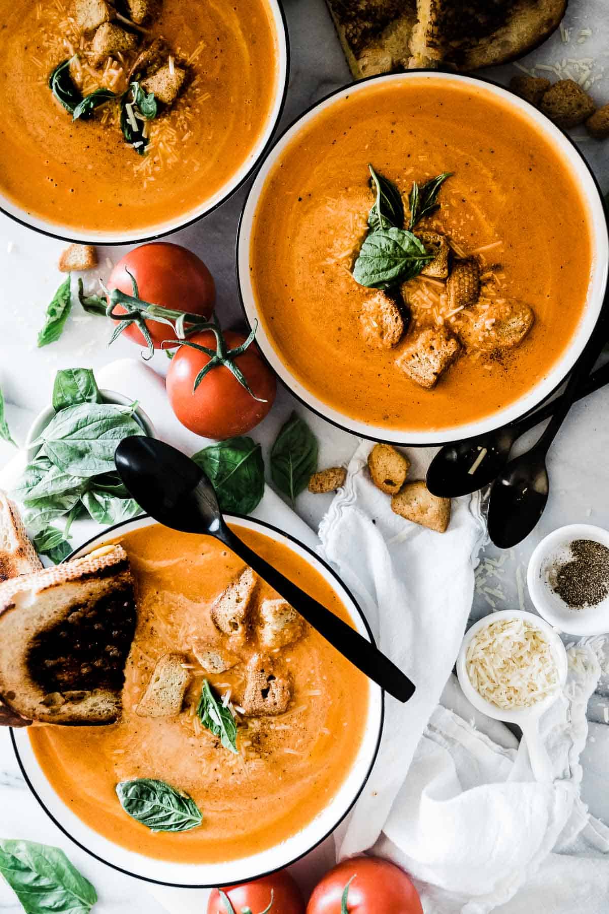 Instant pot tomato soup in white bowls with black rims. They are garnished with croutons and basil.