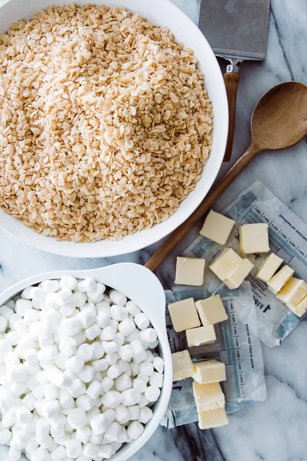 a large bowl of rice krispies, marshmallows, and butter on a marble board. 