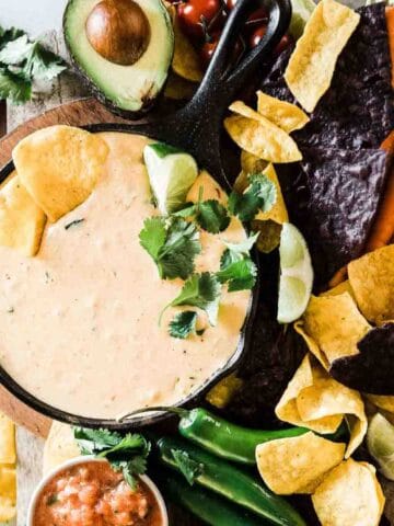 A small skillet of cafe rio copycat queso recipe on the table with chips, salsa and guacamole.