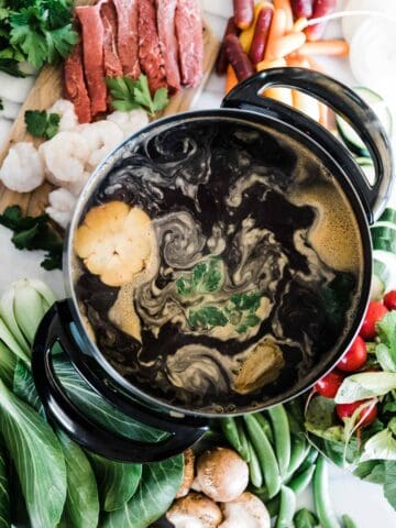 Broth fondue simmering in a fondue pot surrounded by veggies and meats.