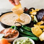 The best queso recipe in a cast iron skillet. The dip is being dunked into with a tortilla chip.