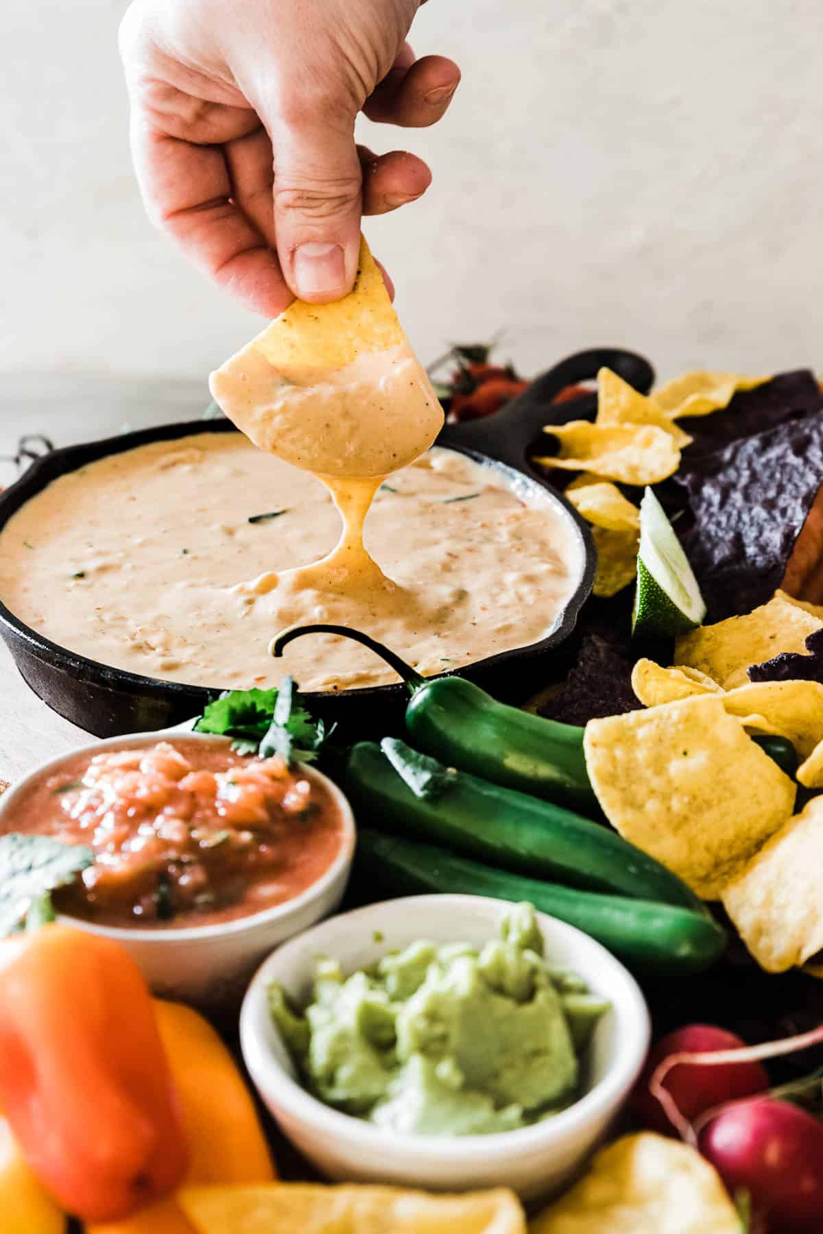 The best queso recipe in a cast iron skillet. The dip is being dunked into with a tortilla chip.