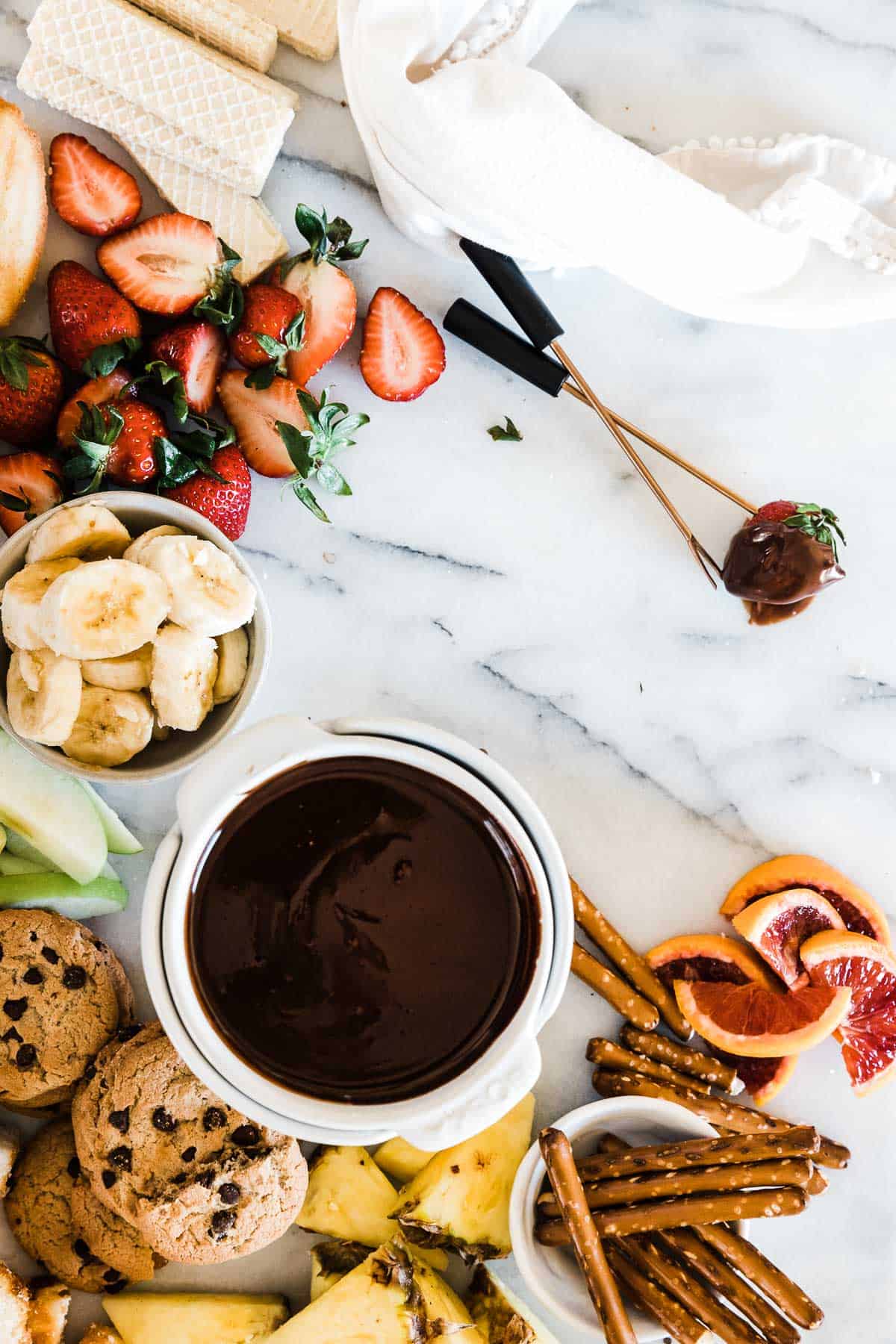 Chocolate fondue in a white dish surrounded by dippers.