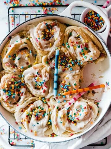 Birthday cake cinnamon rolls in a white braiser. They are topped with sprinkles and birthday candles.