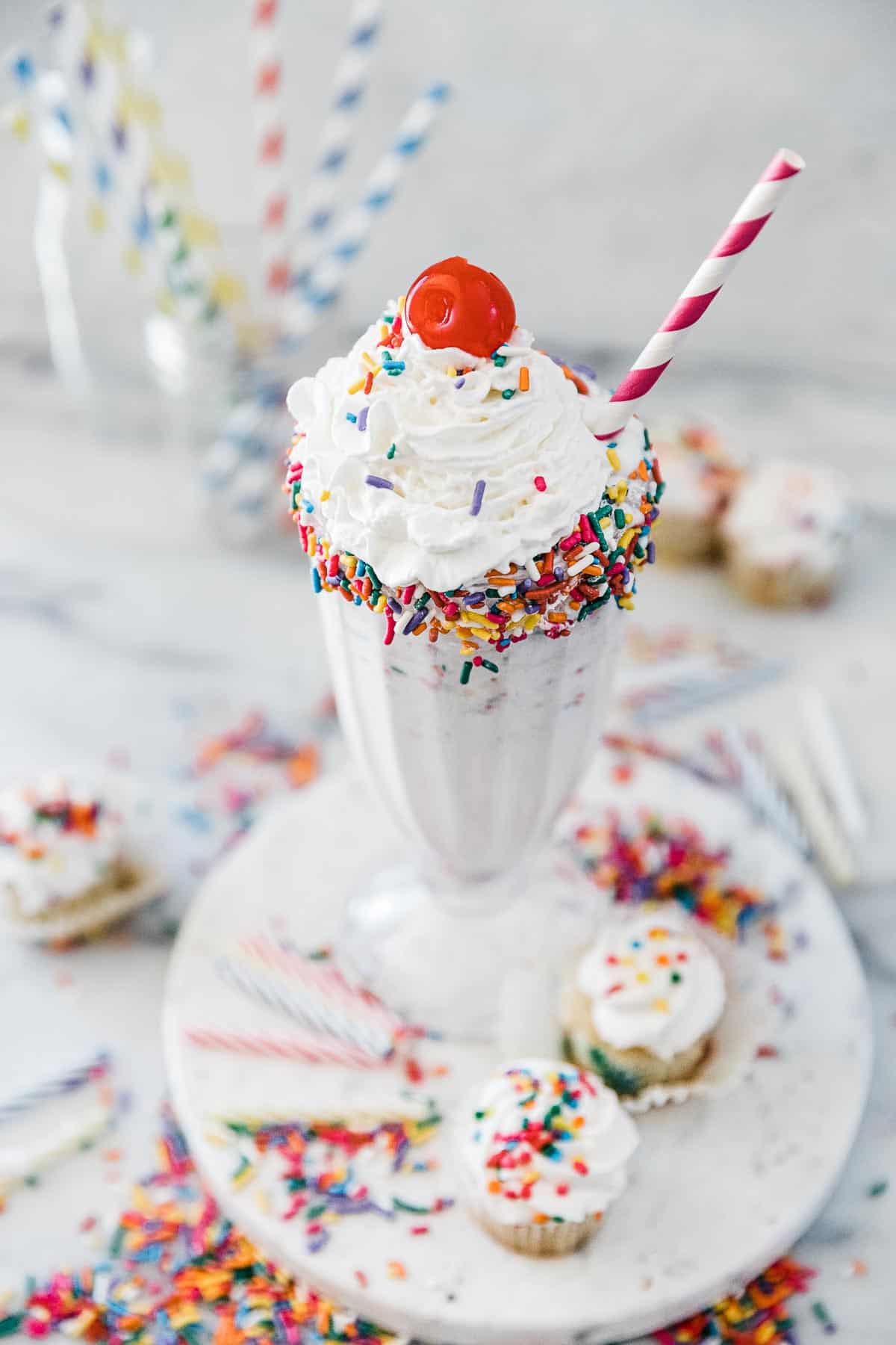 Cake shake in a Sunday glass topped with whipped cream and a cherry.