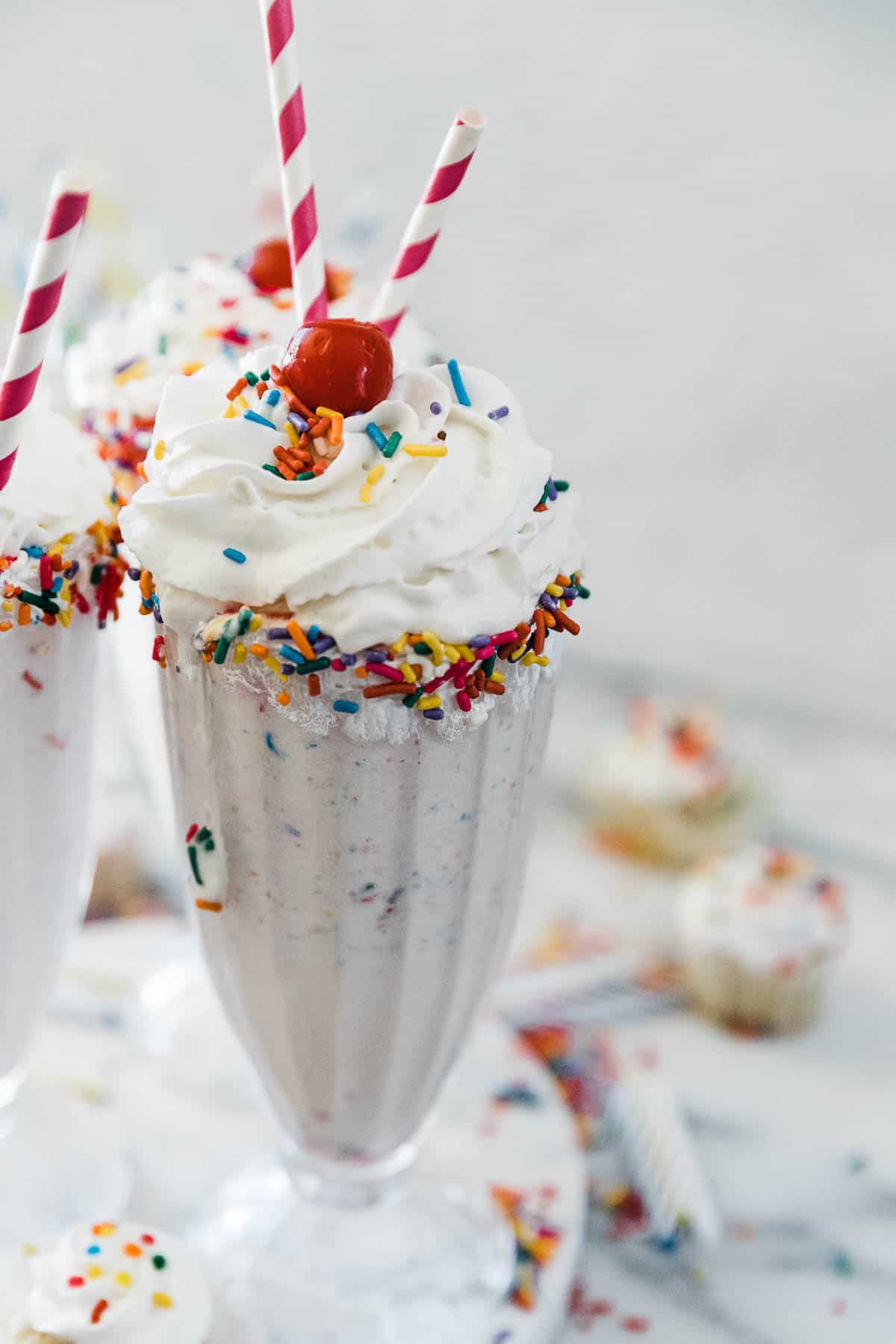 A half shot of cake shake in a Sunday glass rimmed with sprinkles.