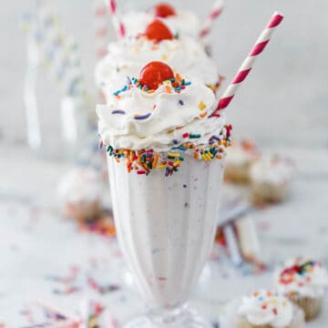 Three glasses of cake shake stacked in a row. They are topped with whipped cream.