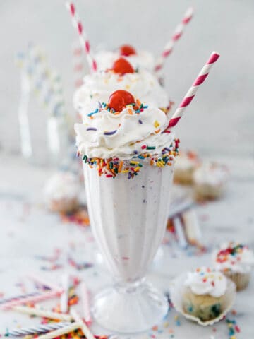 Three glasses of cake shake stacked in a row. They are topped with whipped cream.