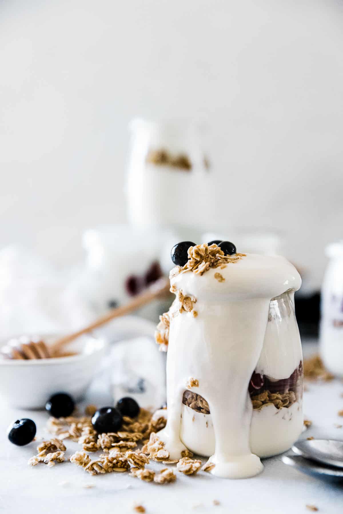 A glass jar filled with pressure cooker yogurt, granola, and berries. There is a bowl of honey to the side.
