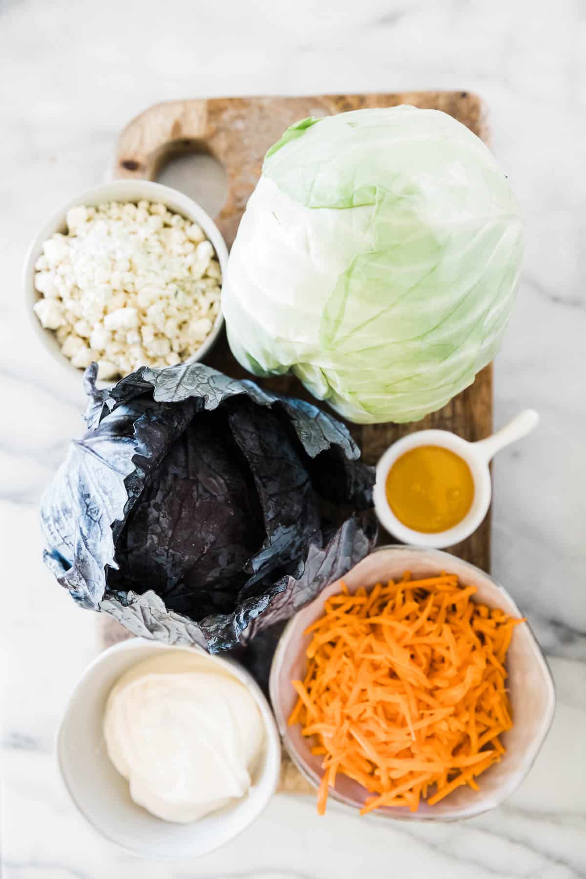 Ingredients needed to make coleslaw on a wooden cutting board - cabbage, carrots, and dressing.