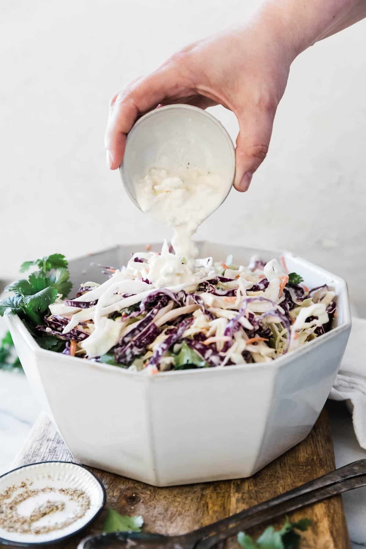 Blue cheese coleslaw in a white bowl. Blue cheese dressing is being poured on top.