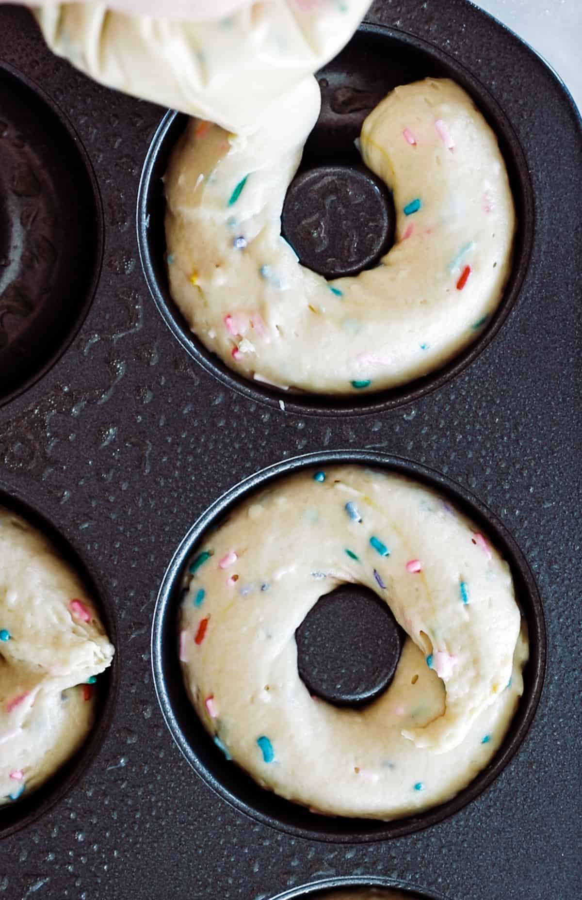 Piping in batter into the donut pan. 
